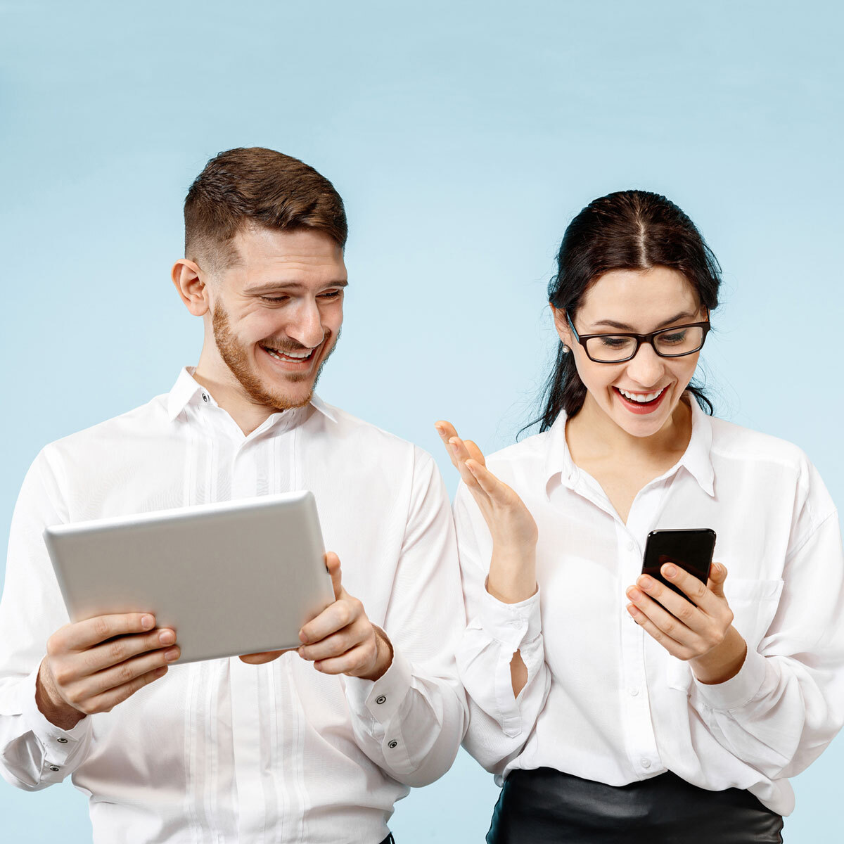A woman looking at her phone with excitement and a man next to her holding a tablet looking at the woman's phone with a happy face as well.