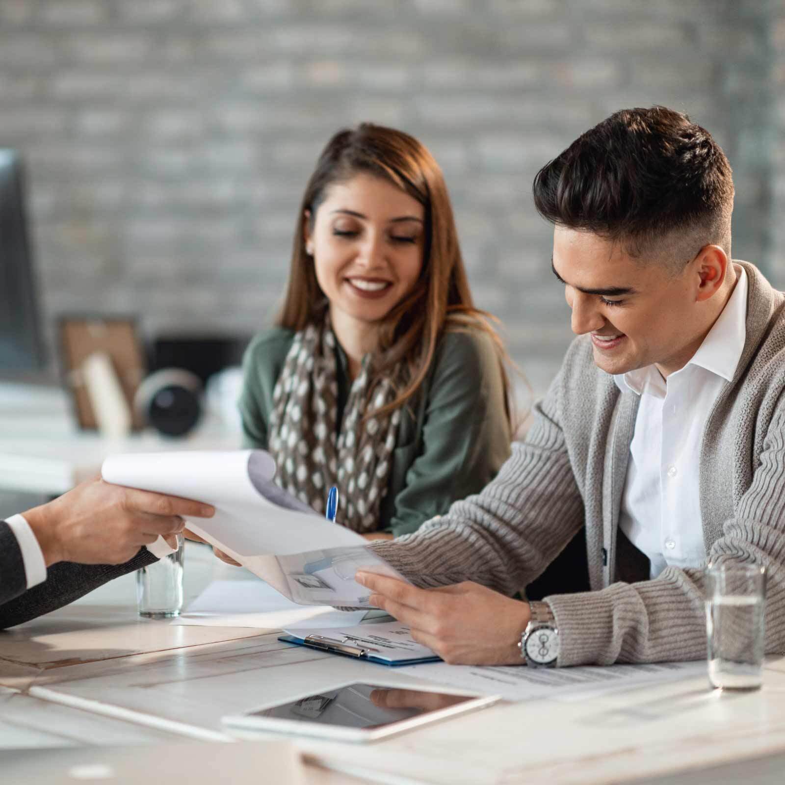 Smiling couple reviewing documents with a professional at an office desk.